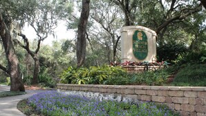 A stone sign with the text "Summer Beach Village" surrounded by a garden with purple flowers and a stone wall.