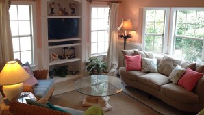 A living room with a sofa, a glass coffee table, a television on a shelf, and a lamp.