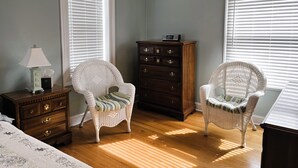 A bedroom with two wicker chairs, a dresser, and a bedside table with a lamp.
