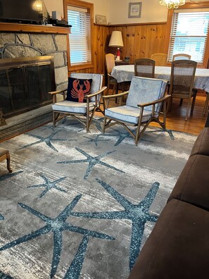 A living room with a stone fireplace, wooden walls, a star-patterned rug, and a dining area with a table and chairs. - 1/2 Block to Beach- Spring Lake Border- Great for Families, easy walk to Beach (Belmar)