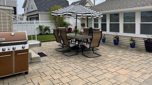 A patio with a barbecue grill, outdoor table and chairs, and a striped umbrella.