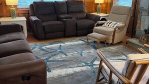 A living room with a sectional sofa, a recliner, a small table with a lamp, and a stone fireplace.