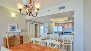 Un comedor con una mesa de madera y sillas blancas, un candelabro y una cocina al fondo.