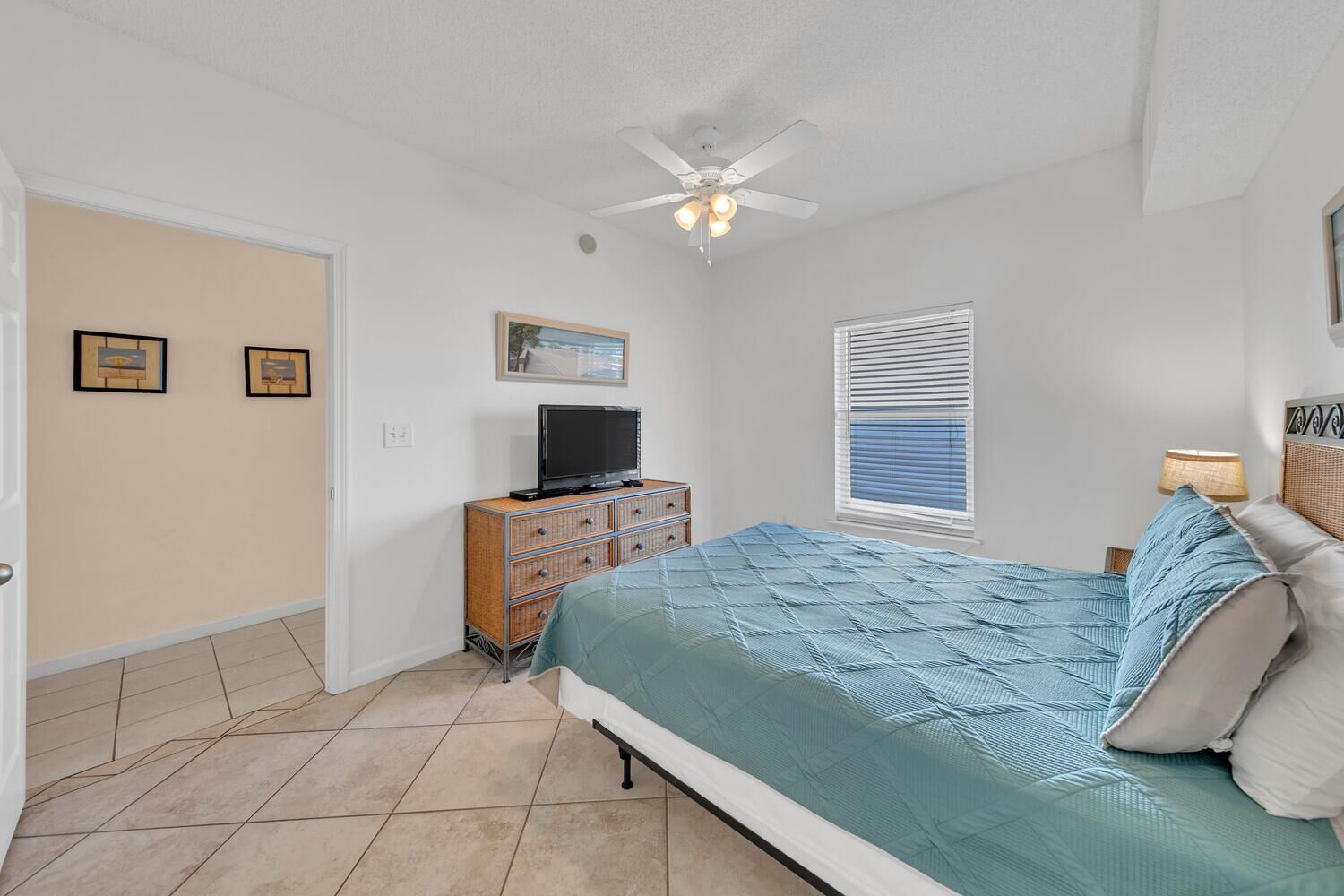 A bedroom with a bed, a dresser, a television, a ceiling fan, and a window with blinds.