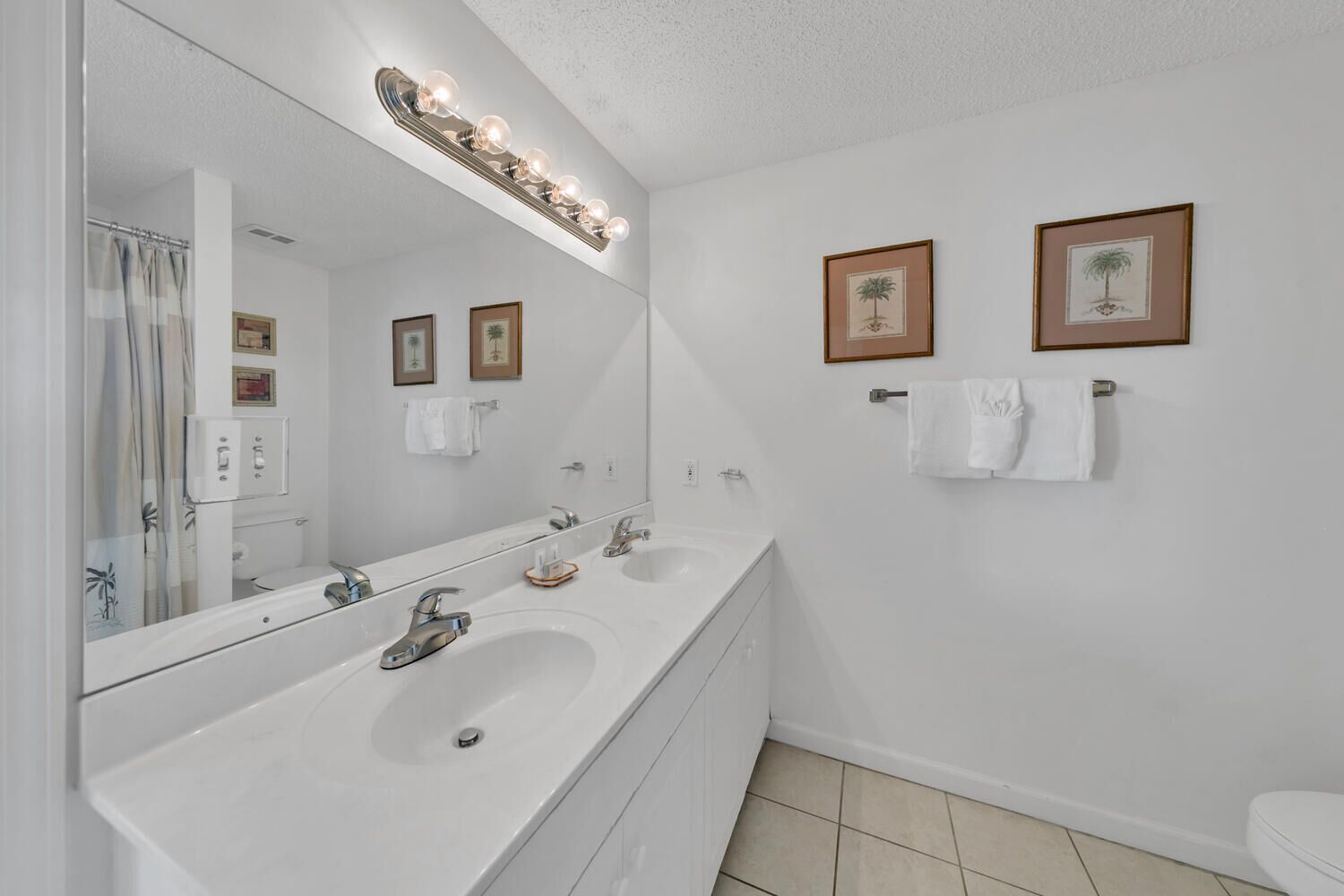 A bathroom with two sinks, a large mirror, and framed pictures on the wall.