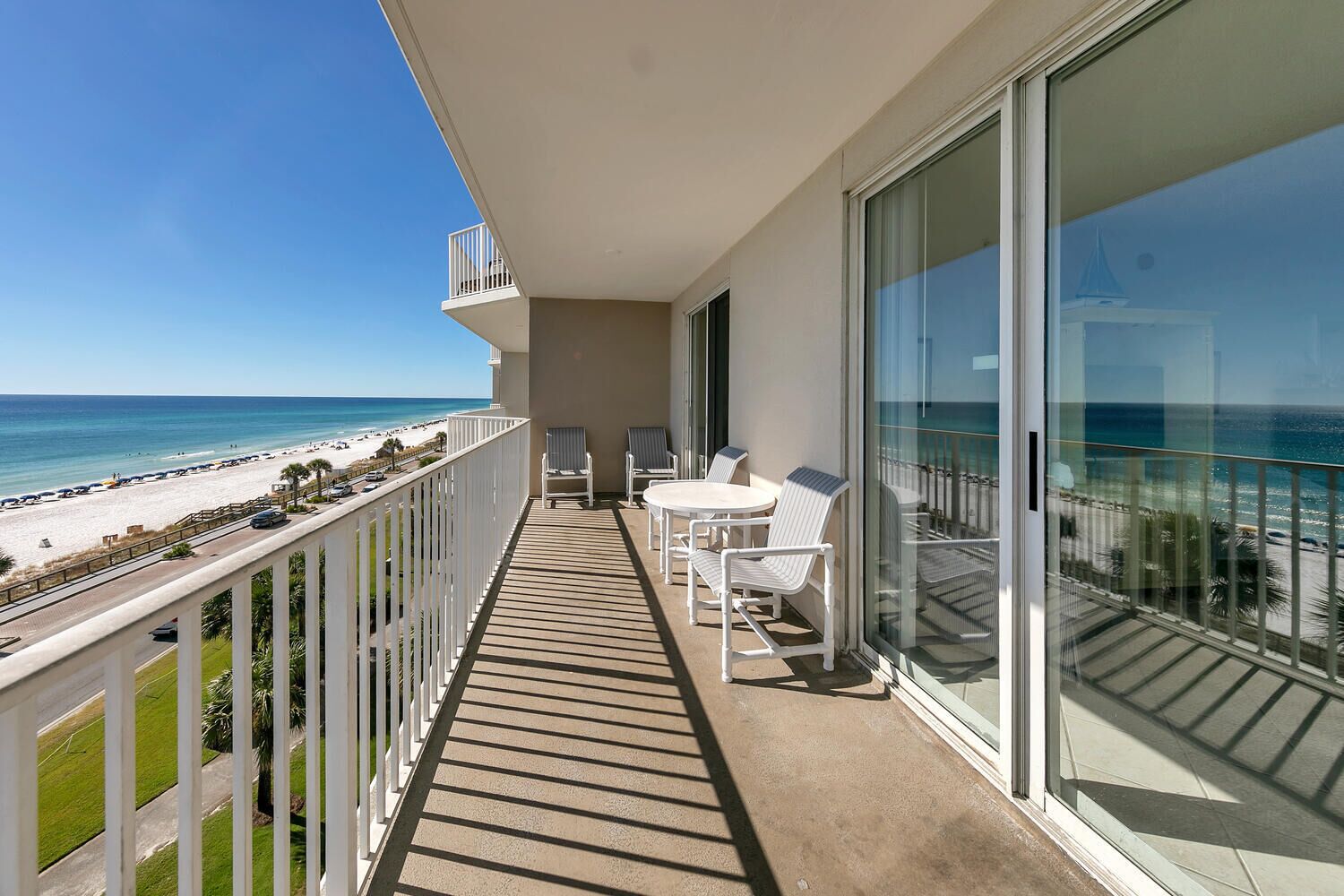 A balcony with a view of the beach, a table, and two chairs.
