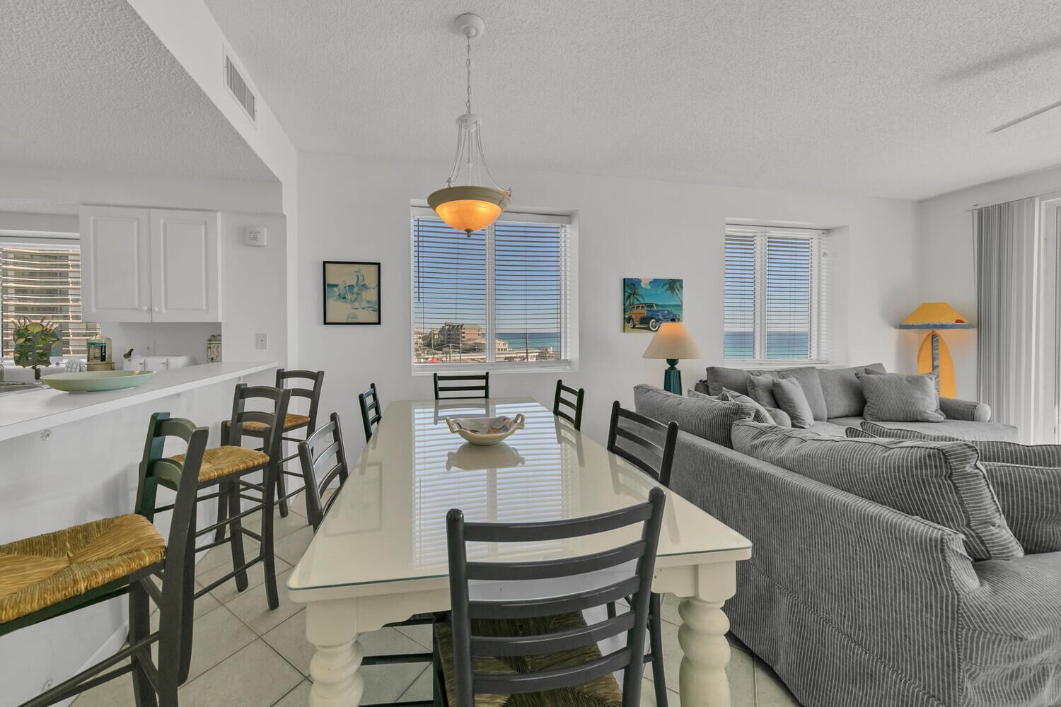 A modern kitchen with white cabinets, a dining table with chairs, and a large window with blinds.