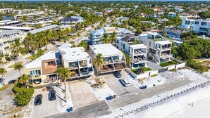 Un quartier résidentiel en bord de mer, avec des maisons modernes, une piscine et une plage au premier plan.