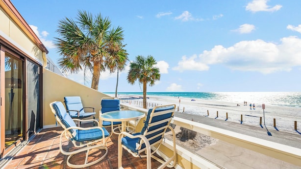Un balcon avec vue sur la plage, comprenant des chaises longues et une table.