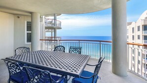 A balcony with a table and chairs, a view of the ocean, and a building in the background. - Beach Colony West 17F Penthouse/Gulf Front 3BR & Beach Service (Navarre)