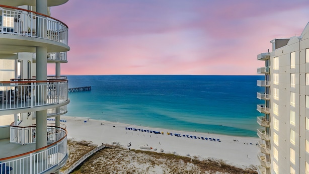 A beachfront hotel with multiple balconies, a pier, and a beach with umbrellas. - Beach Colony West 17F Penthouse/Gulf Front 3BR & Beach Service (Navarre)