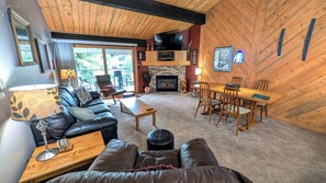 A cozy living room with a fireplace, leather sofa, wooden dining table, and a TV mounted on the wall. - Luxury Condo w/ FREE WiFi, Parking, Heated Pool, Hot Tubs, Skier Shuttles (Avon)