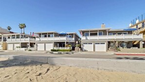 A beachfront hotel with multiple balconies, a sandy foreground, and a clear blue sky.