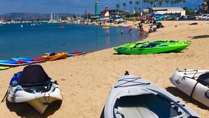 A beach with kayaks, a lighthouse, and palm trees.