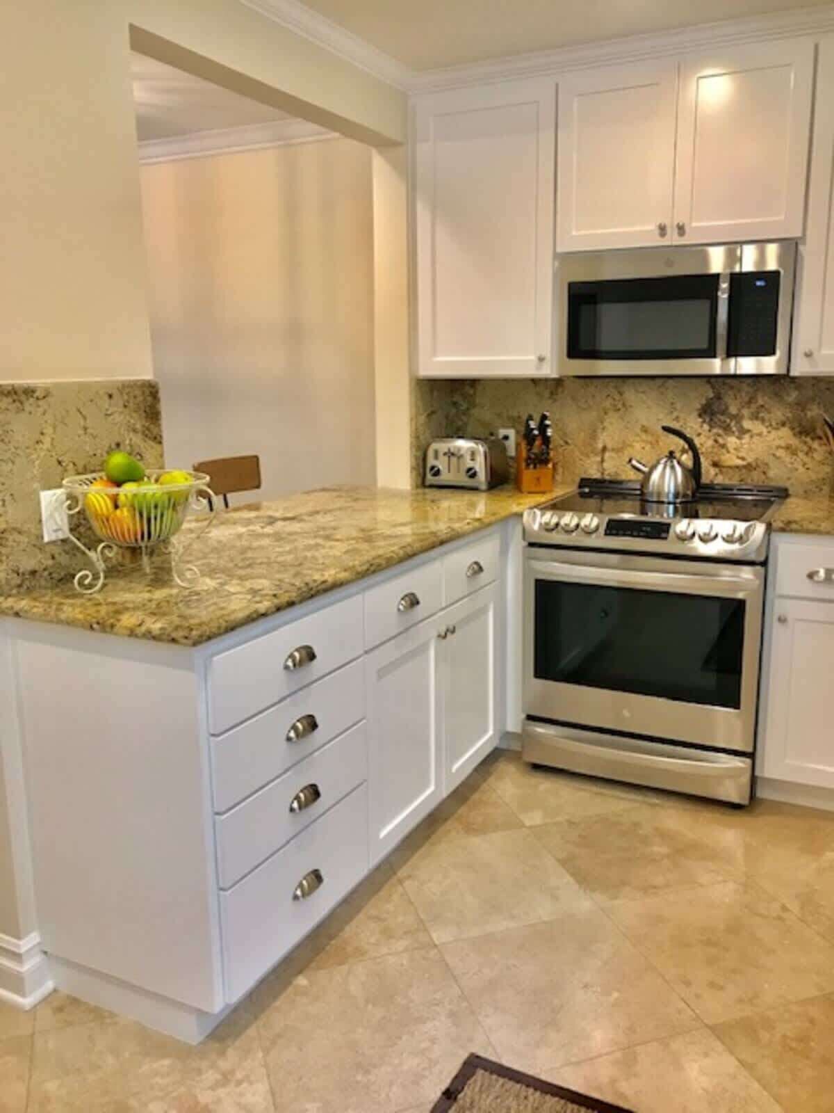 Una cocina con armarios blancos, encimera de granito, estufa de acero inoxidable y microondas.