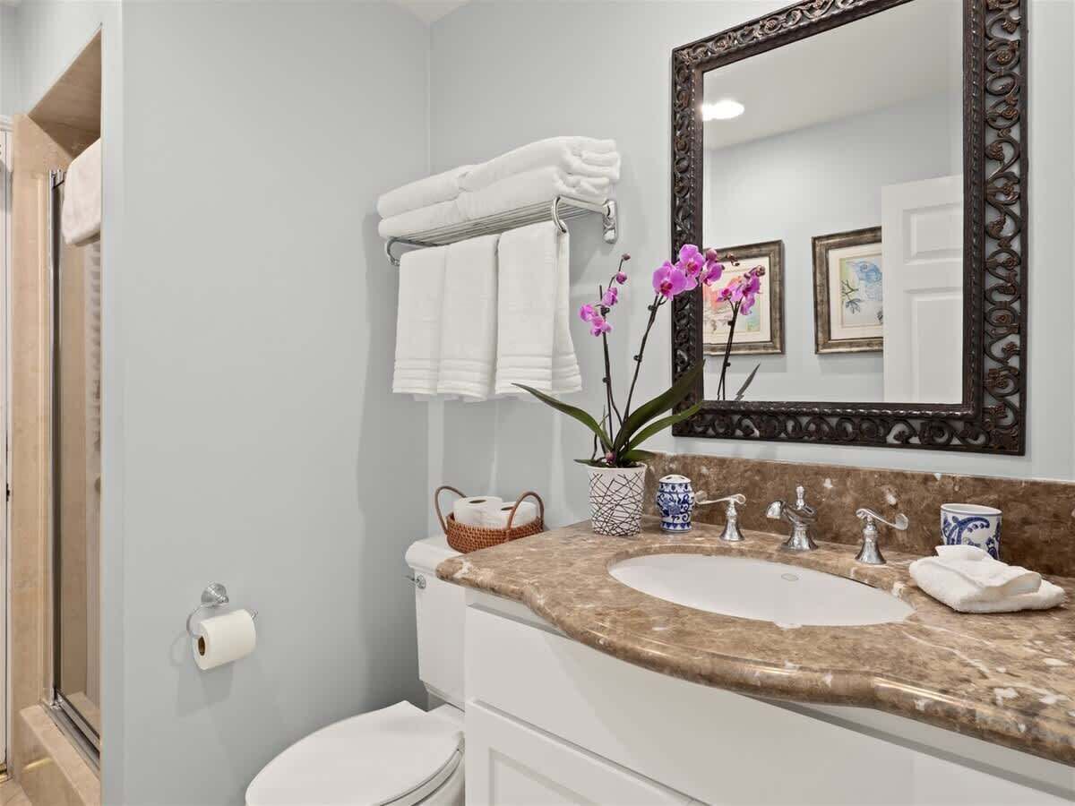 Un baño con encimera de mármol, lavabo, inodoro, toallero y espejo.