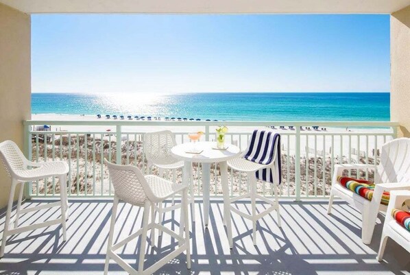 A balcony with a view of the beach, white wicker chairs, a small round table, and a striped towel.