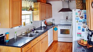 A kitchen with wooden cabinets, a double sink, a stove, and a refrigerator adorned with magnets. - Island Serenity- Island Time Up in Old Town  (Port Aransas)