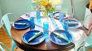 A dining table set with blue plates and glasses, surrounded by turquoise chairs, with a window and wall decorations in the background. - Island Serenity- Island Time Up in Old Town  (Port Aransas)