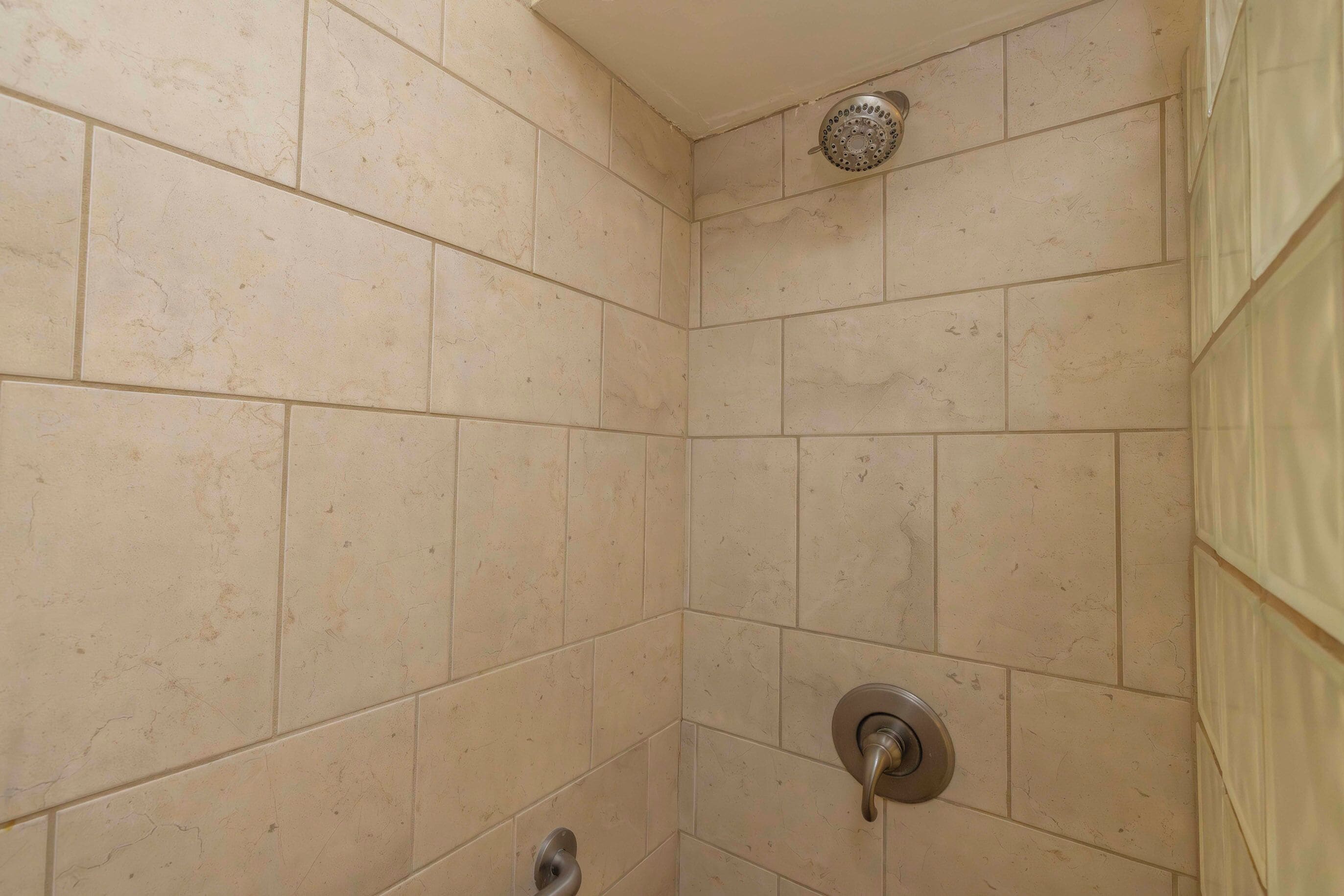 A corner of a bathroom with beige tiles, a showerhead, and a faucet.