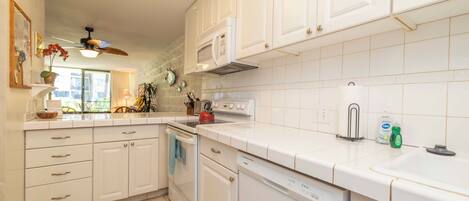 A kitchen with white cabinets, a microwave, a kettle, and a dishwasher.
