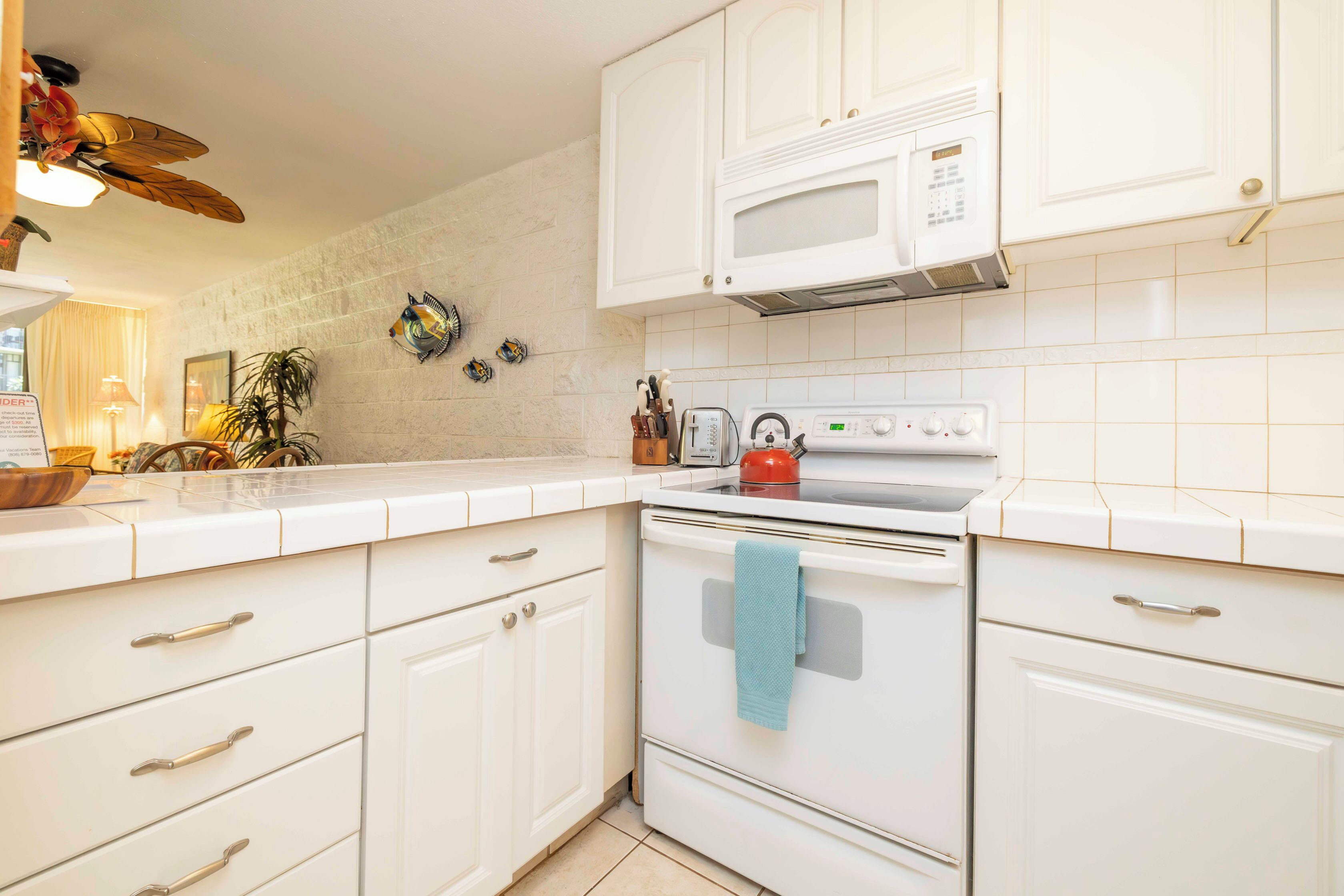A kitchen with white cabinets, a microwave, a stove, and a blue towel hanging on the oven.