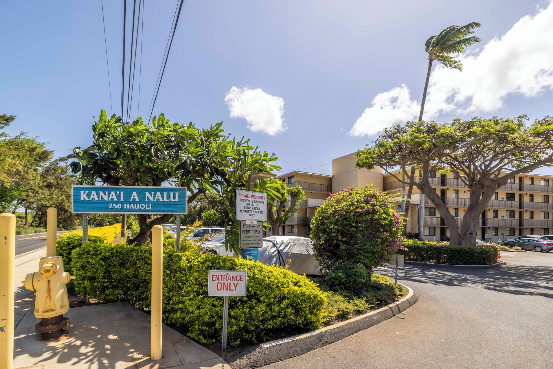 Une vue de rue avec une enseigne indiquant « Kana’i A Nalu », située au 250 Hawaii, ainsi qu’une pancarte indiquant qu’il s’agit d’une propriété privée, une autre indiquant un espace de stationnement et une dernière signalant l’entrée.