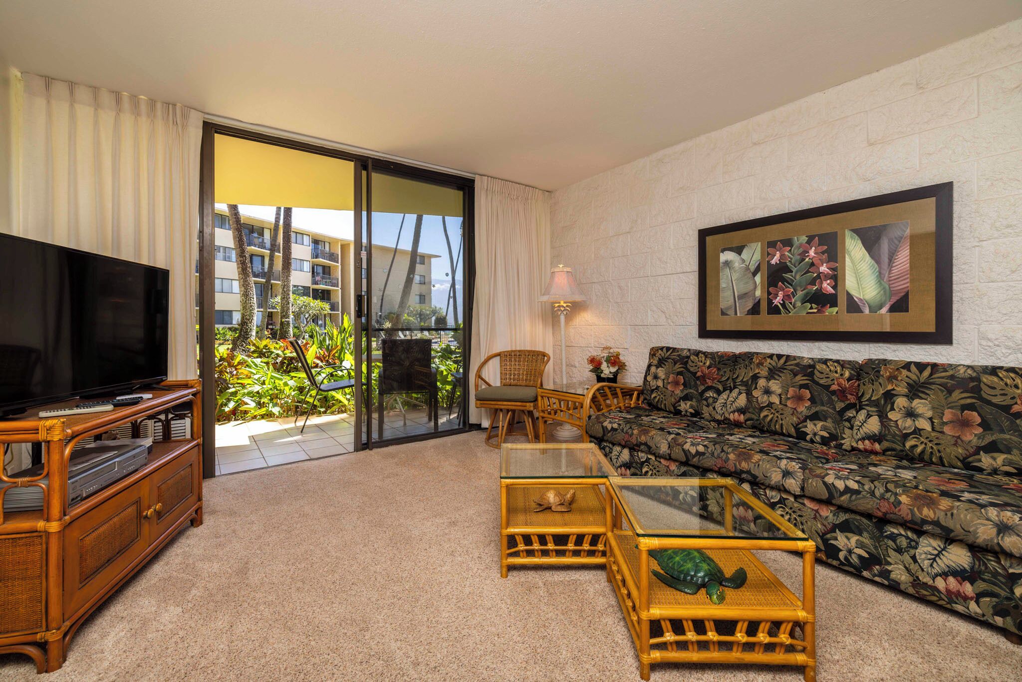 A living room with a television, sofa, and coffee table, a balcony with plants, and a framed picture on the wall.