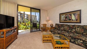 A living room with a television, sofa, and coffee table, a balcony with plants, and a framed picture on the wall.