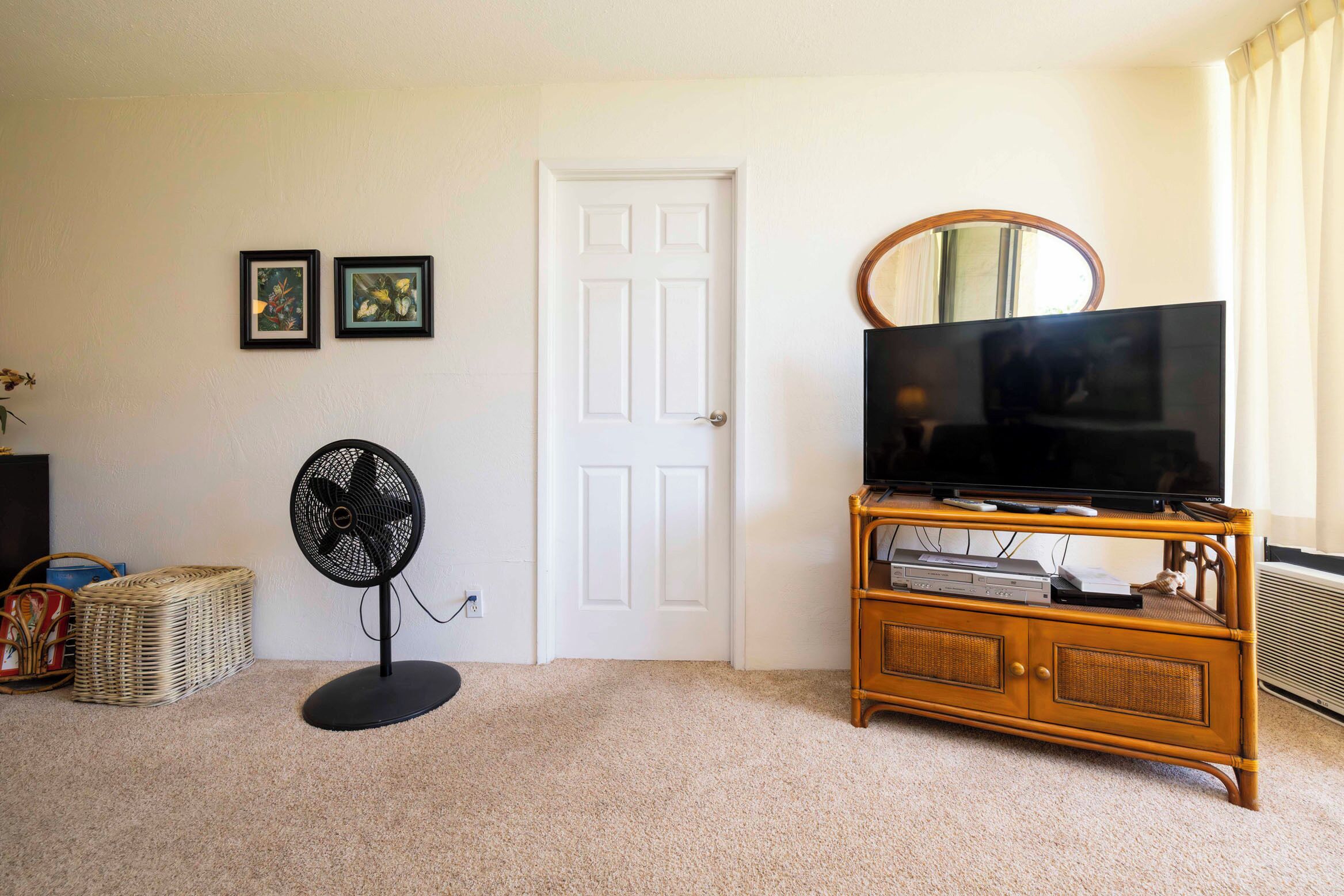 Ein Zimmer mit Fernseher auf einem Holztisch, einem Standventilator und zwei gerahmten Bildern an der Wand.
