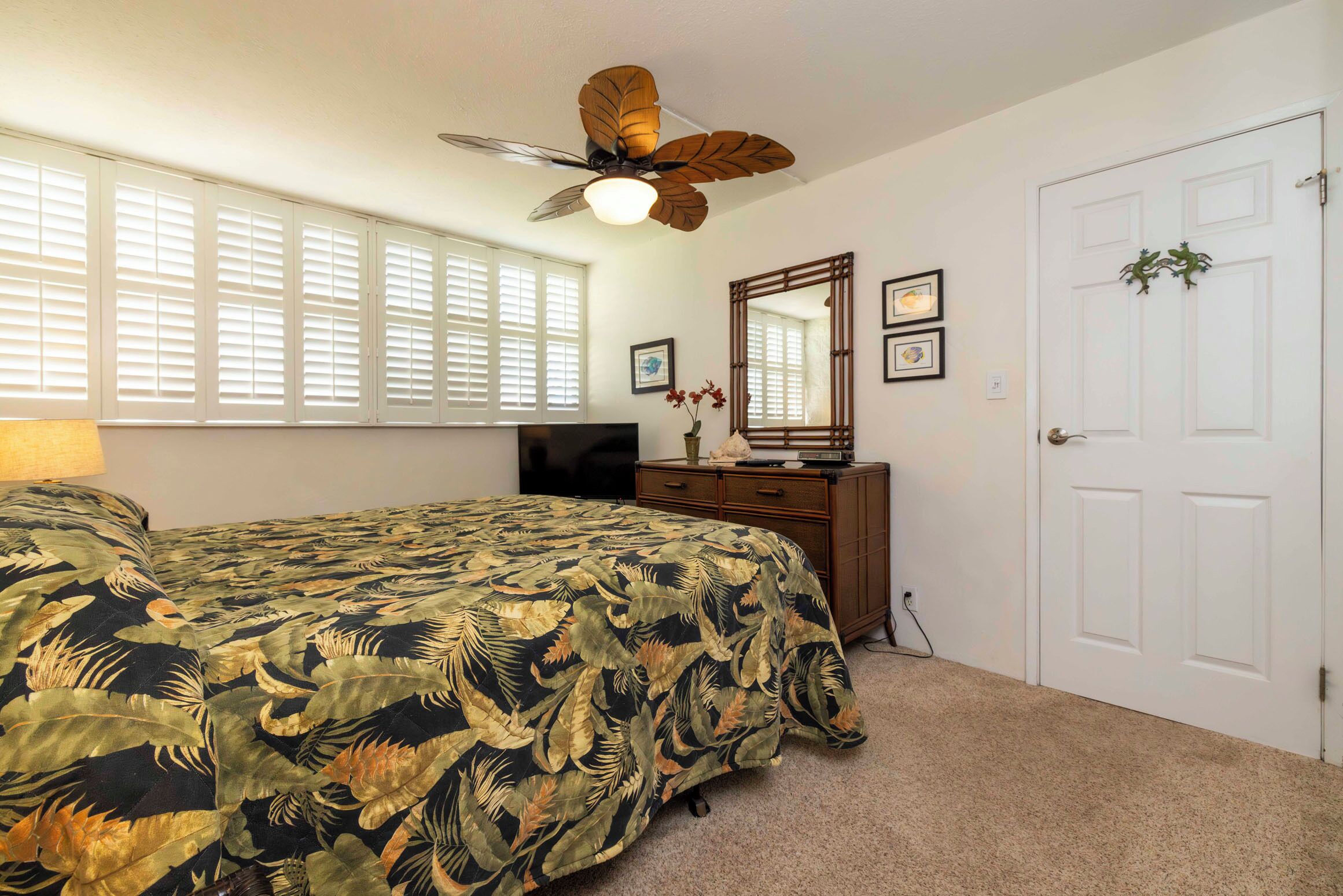 A bedroom with a bed, a ceiling fan, a dresser, a TV, and a door with a mirror and decorations.