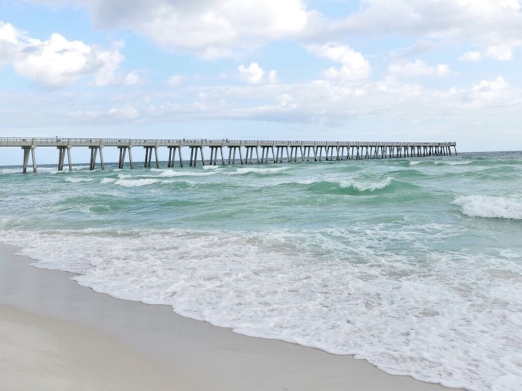 A beach with waves and a pier extending into the ocean.