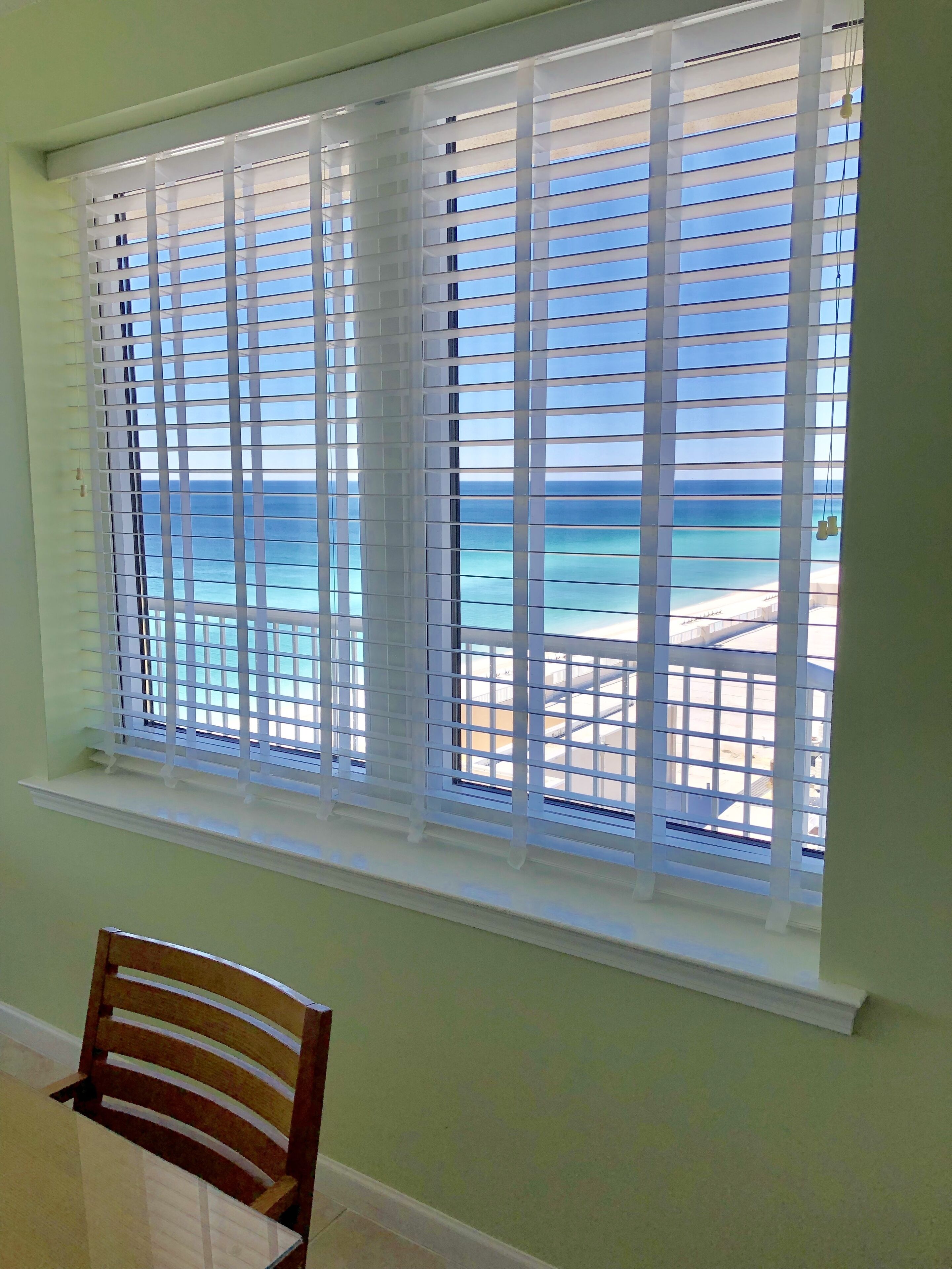 A room with a window overlooking a beach, a wooden chair, and a white window sill.