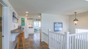 A kitchen with a bar area, white railings, and a hanging light fixture. - 4759- Sun Daze - Ocean Views, Pool, Hot Tub & Steps to Beach (Kitty Hawk)