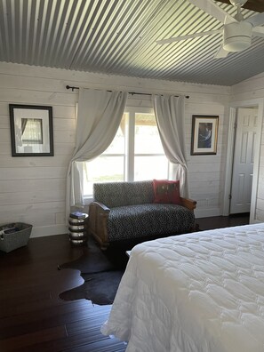 A bedroom with a bed, a window with curtains, a couch, and a ceiling fan.