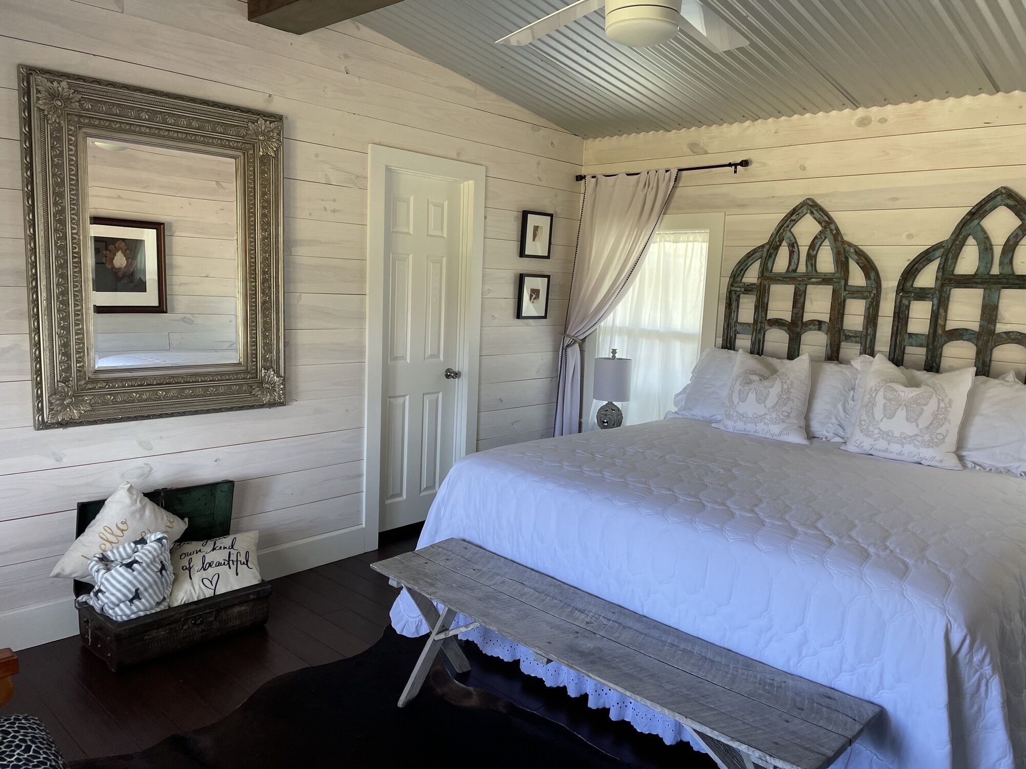 A bedroom with a large bed, a wooden bench, a dresser, and a mirror.
