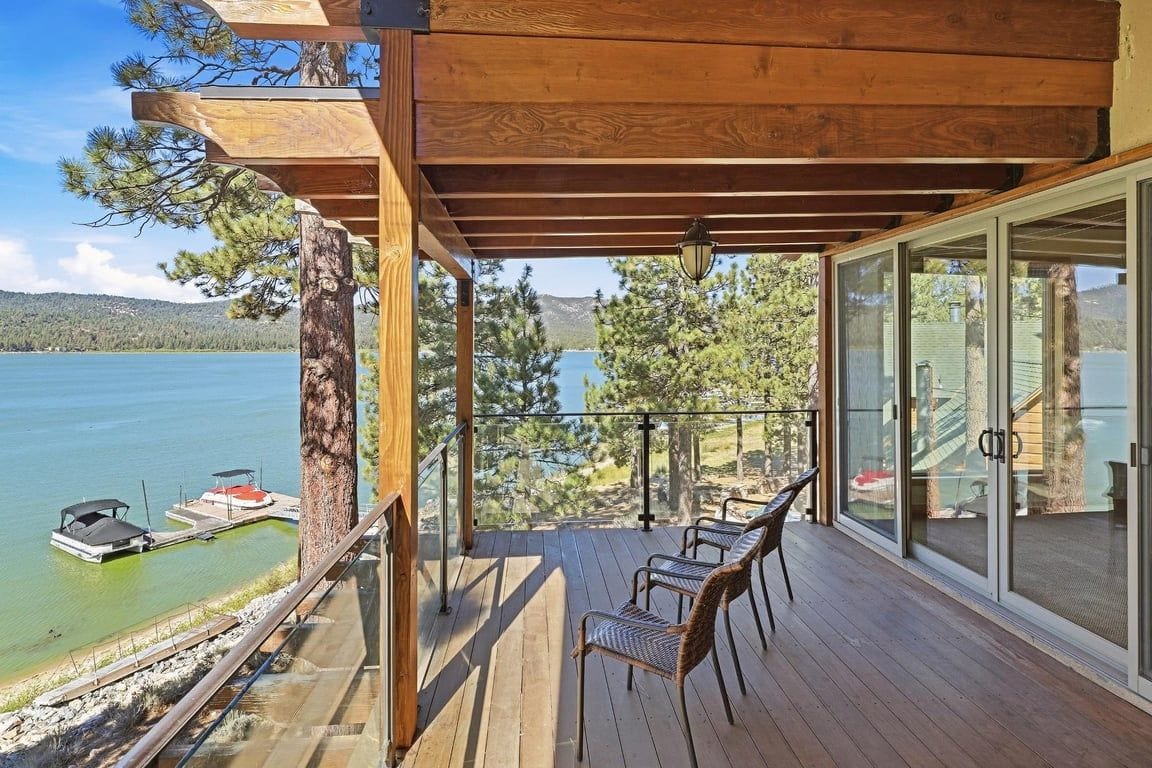 Eine Holzterrasse mit Glastrennwand, die auf einen See blickt, mit Stühlen und Blick auf Boote.