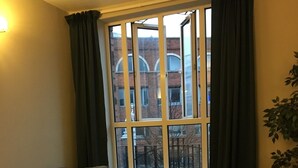 Un soggiorno con un tavolino in vetro, un divano in pelle e vista sugli edifici attraverso una finestra con tende.