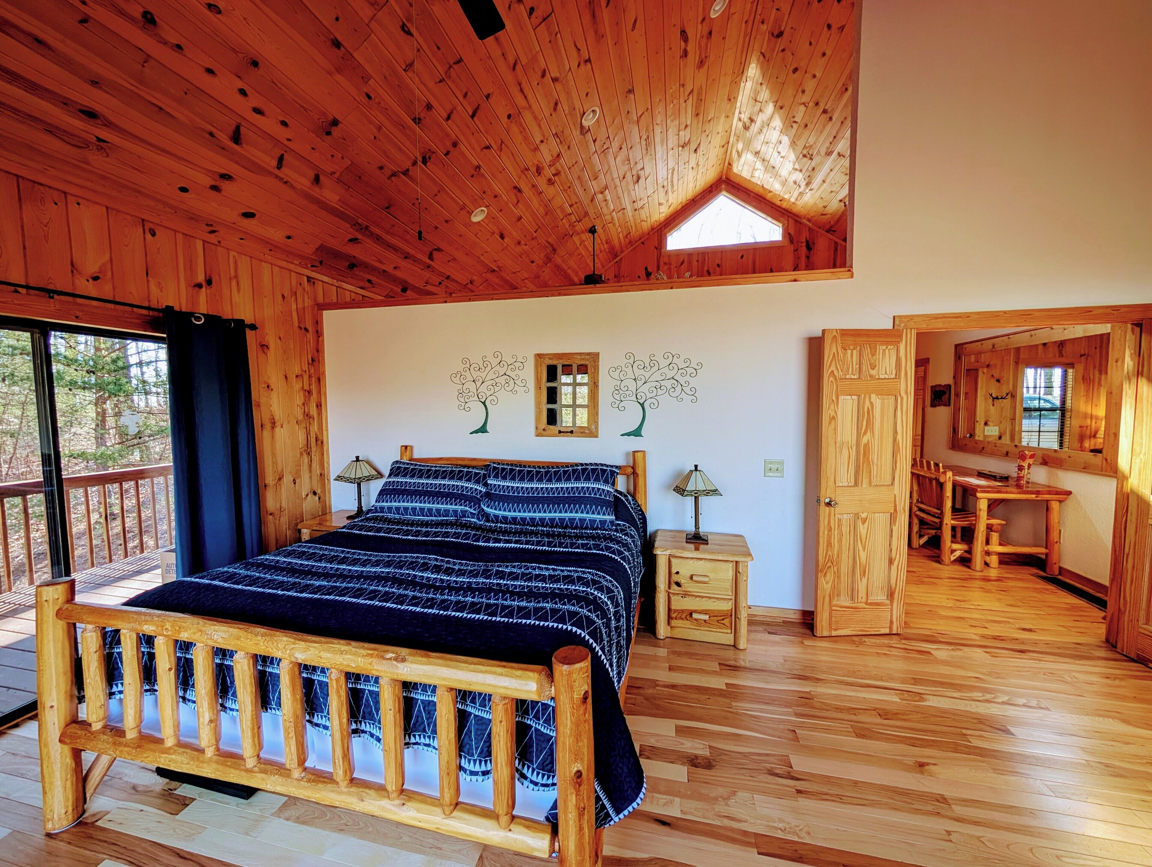 A wooden cabin bedroom with a bed, bedside tables, a desk, and a chair.