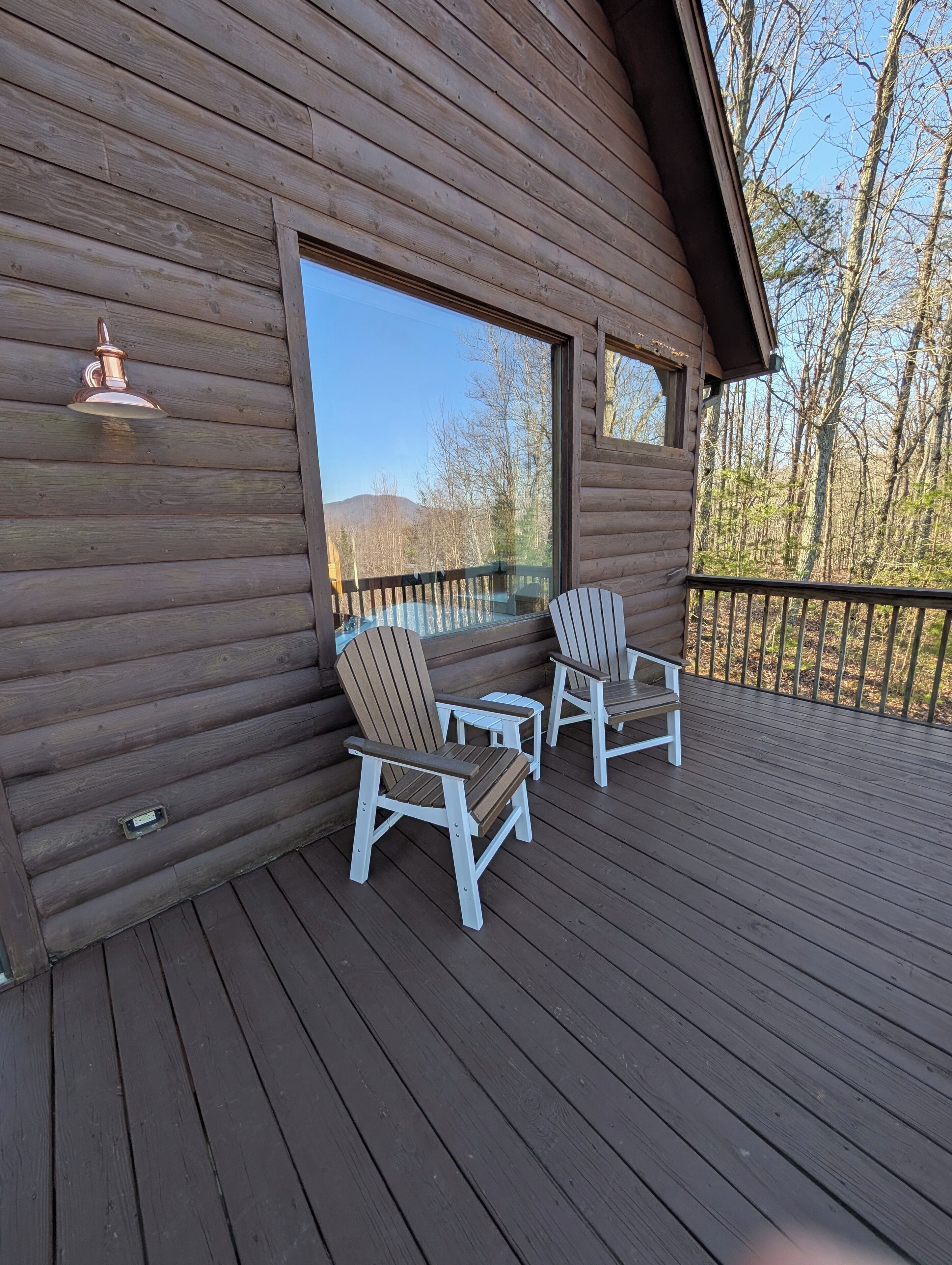 A wooden deck with Adirondack chairs and a large window overlooking a forested area.