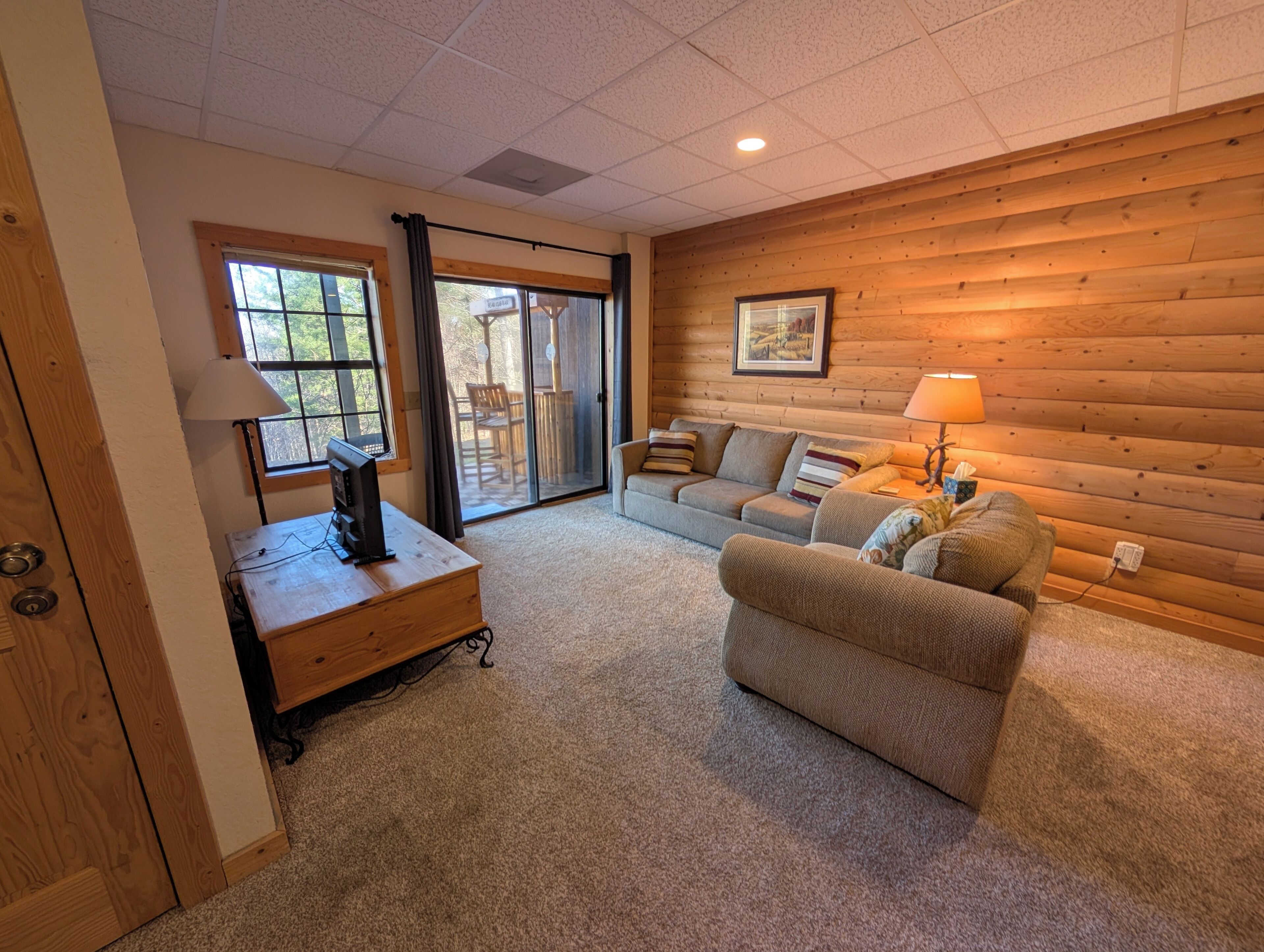 A cozy living room with a wooden wall, a sofa, a coffee table, and a TV.