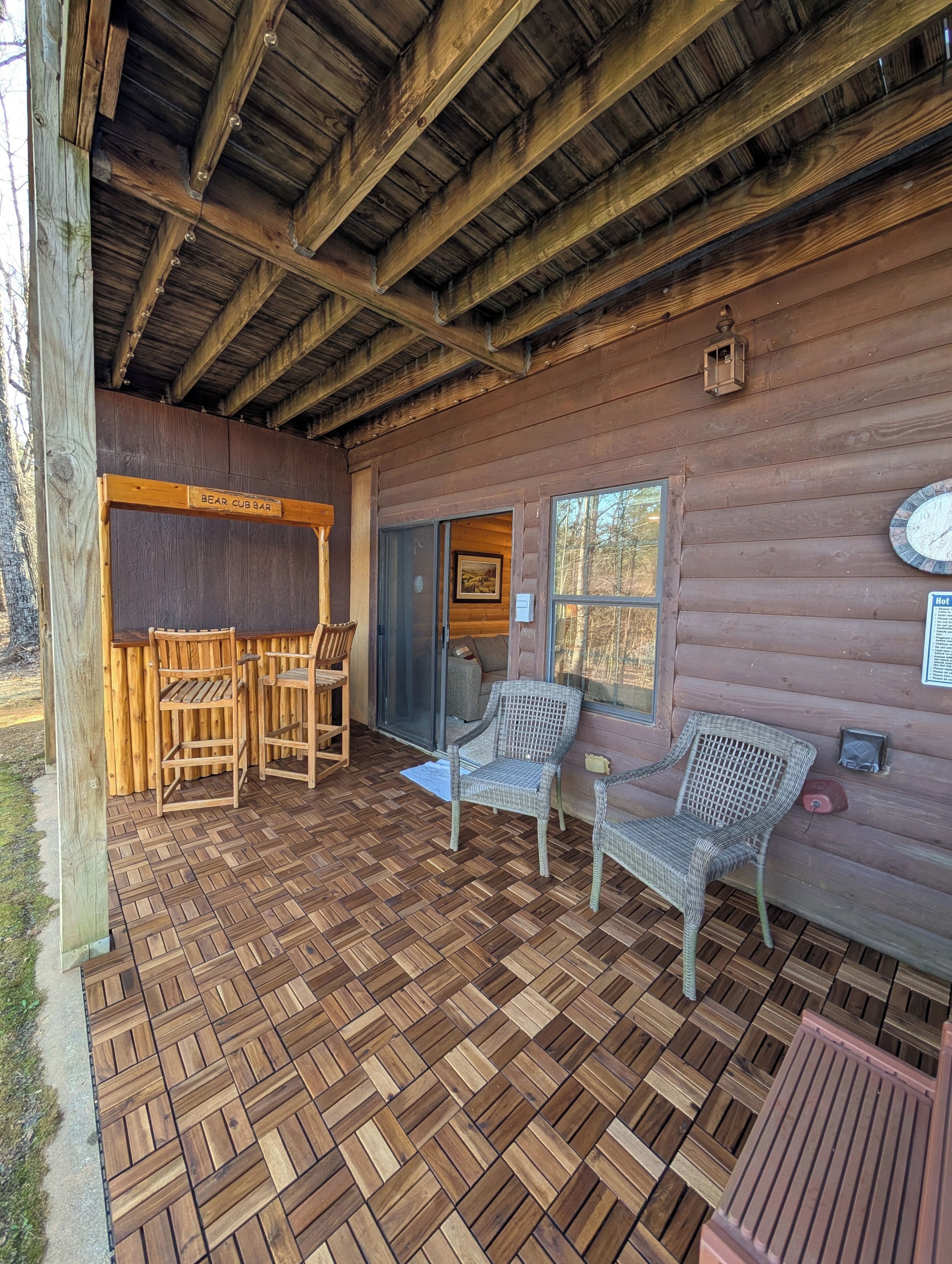 A wooden cabin with a herringbone-patterned floor, a bar area, wicker furniture, and a clock on the wall.