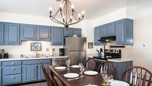 A modern kitchen with blue cabinets, a stainless steel refrigerator, a dining table set for four, and a chandelier. - Family Home in Town, Across from Rio Grande Trail (Glenwood Springs)