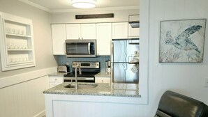 Una cocina moderna con armarios blancos, un refrigerador de acero inoxidable y un microondas. Hay una silla de cuero negro en primer plano.