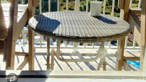 Mesa y sillas de mimbre en un balcón con vista al océano y árboles.