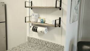 Una cocina con encimera de granito, tres estantes de madera, una silla negra y un refrigerador.