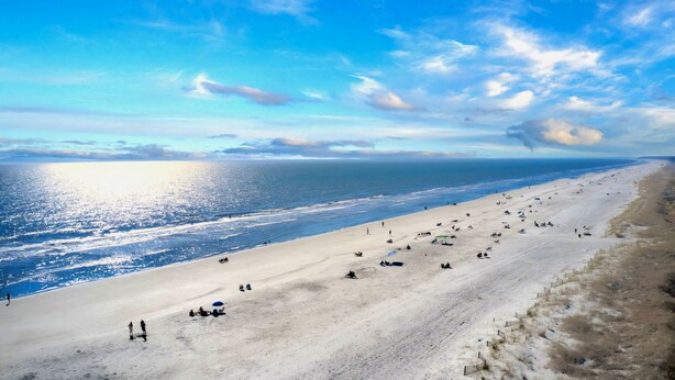 Una playa extensa con gente tomando el sol y paseando por la orilla.