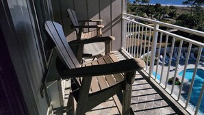 Un balcón con dos sillones de descanso y una mesita pequeña, con vista a una piscina y una playa.