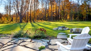 A stone patio with a white Adirondack chair, surrounded by a grassy lawn and a forest with autumn foliage. - Location!!! Location!!! Berkshire Glamour (and comfort) Meets Town And Country (Stockbridge)