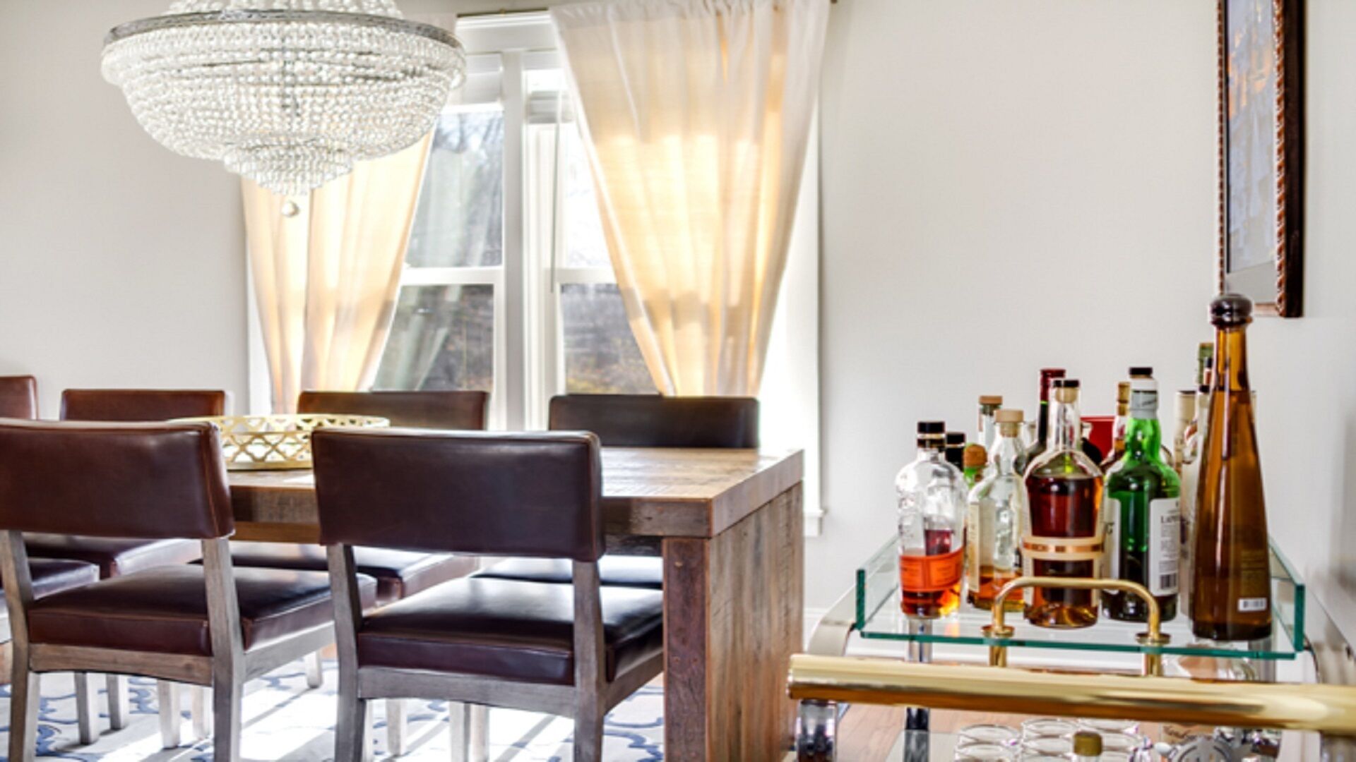 Un comedor con mesa de madera, sillas de cuero, candelabro y vitrina de vidrio con botellas de licor.